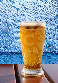 Beer glass on wooden table taken closeup on blue water drips background.