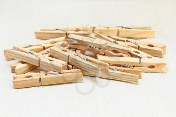 Wooden clothespins heap taken closeup on white fabric background.