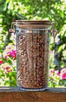 Coffee beans in glass container taken closeup on floral background.