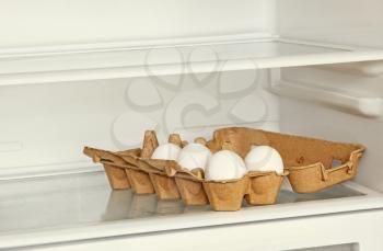 Fresh eggs in a paper box on refrigerator shelf taken closeup.