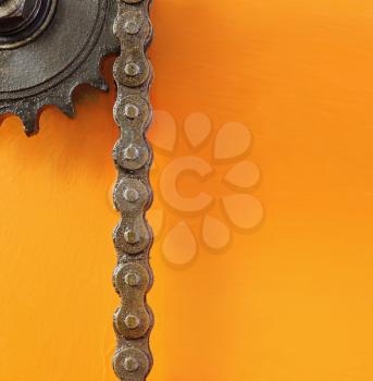 Black metal cogwheel and chain on orange background with empty space for text.