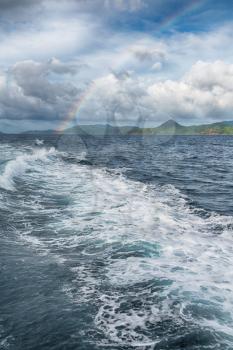 from a boat the rainbow from  ocean and island in background