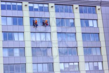Two workers of steeplejack washing a skyscraper windows