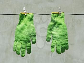 Two vividly green gloves hanging on a wire on a background of gray wall in bright sunlight
