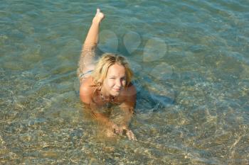 Beautiful smiling teenage girl lying in the shallow coastal sea water with pebbly bottom