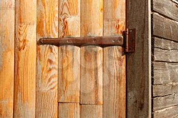 Wooden door of the old barn hanging on long iron hinge close-up, in bright sunlight