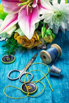 sewing accessories with bouquet of fresh flowers on turquoise background