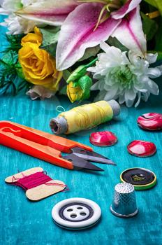 sewing accessories with bouquet of fresh flowers on turquoise background