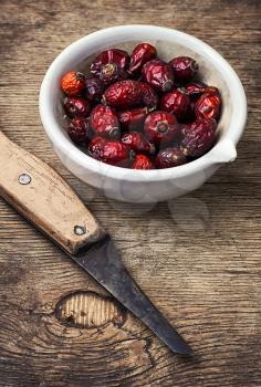 dish of dried medicinal rose hips on background of knife in rustic style
