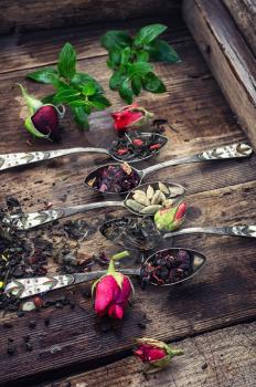 Dry tea leaves in spoons with small buds of roses in  wooden box