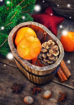 Wooden bucket with tangerines and pine cones on the background of Christmas trees and spices