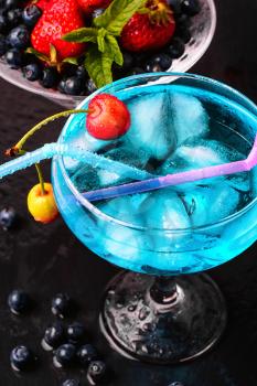 glass of blue alcohol cocktail in glass with cherry