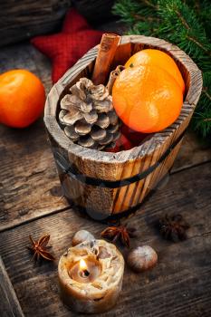 Wooden bucket with tangerines and pine cone and a burning Christmas candle