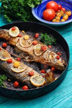 Frying pan with two baked fish in tomatoes,spices and lemon