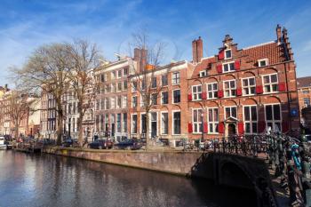 AMSTERDAM, NETHERLANDS - MARCH 19, 2014: Colorful houses along the canal embankment in spring day. Ordinary people walk on the coast
