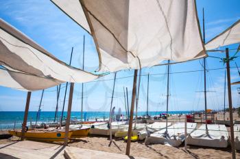 Awnings in sails shape covering relax area near sailing boats on sandy beach in Calafell town, coast of Mediterranean sea, Catalonia, Spain