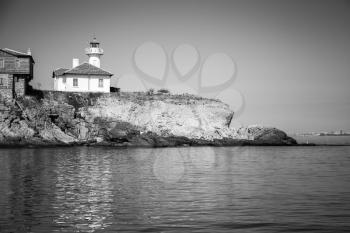 White lighthouse and wooden buildings on St. Anastasia Island. Black Sea, Bulgaria. Monochrome photo