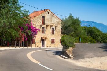Figari, South Corsica. Old rurar house made of stone with red tile roof near asphalt road