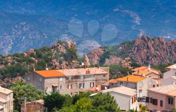 Small Corsican village cityscape, old living houses with red tile roofs over mountains background. Piana, South Corsica, France