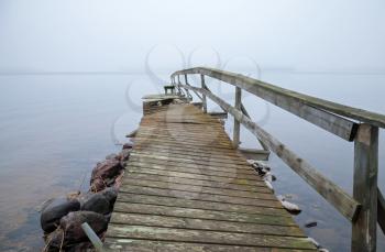 Old broken wooden pier perspective on the lake in foggy morning