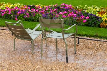 Wet metal armchairs in the rainy park with colorful flowers in Paris