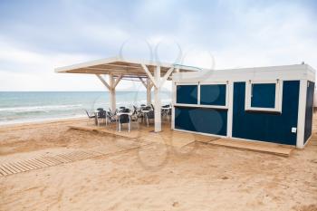 Empty open space bar with wooden floor and metal armchairs on the sandy beach, Mediterranean Sea coast, Spain