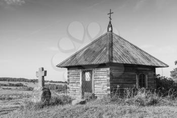 Ancient wooden Orthodox chapel and a stone cross on Savkina gorka, Pskov Region, Russia. Black and white photo