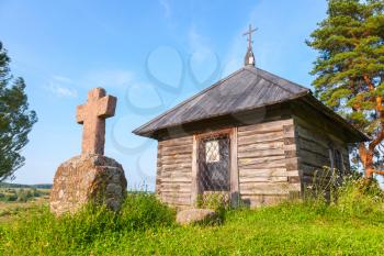 Ancient small wooden Orthodox chapel and a stone cross on Savkina gorka, Pskov Region, Russia