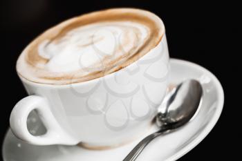 Cup of cappuccino. White mug of coffee with milk foam over black table background, close-up photo with selective focus