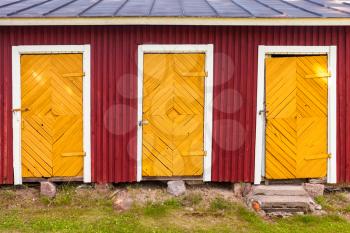 Three yellow locked doors in red rural barn wall, flat background photo texture