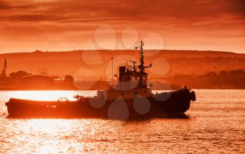 Black sea port at sunset. Tug boat is underway, Varna harbor, Bulgaria. Red toned photo with natural lens flare effect