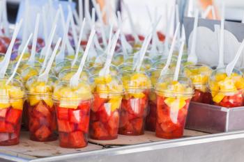 Fresh fruits sorted in plastic cups with forks. Street dessert shop in Lisbon, Portugal. Close-up photo with selective focus