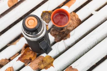 Tourist thermos with cup of tea on white bench in autumn park, top view