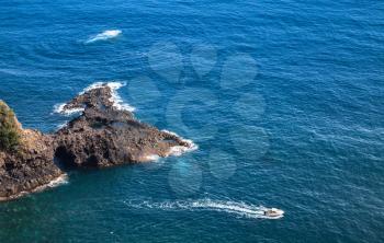 Pleasure motor boat goes near coastal rocks of Madeira island, Bridal Veil Falls viewpoint, Portugal