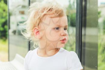 Cute Caucasian blond baby girl waits on a bus stop. Close-up portrait