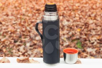 Stainless steel vacuum tourist thermos stands on white table in autumn forest