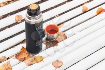 Tourist thermos with cup stands on white bench in autumn park