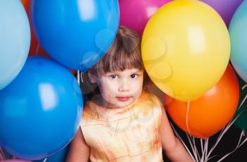 Portrait of Caucasian blond little girl with colorful balloons over black background