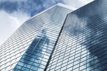 Abstract modern architecture background photo, office tower made of blue glass and steel with reflections of cloudy sky