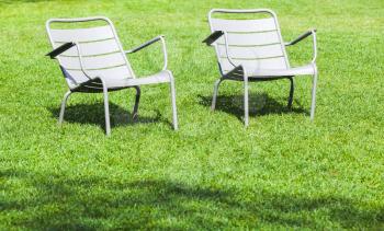 Two outdoor gray metal chairs stand on fresh green grass in summer park