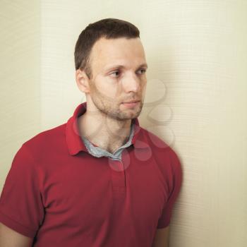 Face studio portrait of young European man in red polo shirt, square frame
