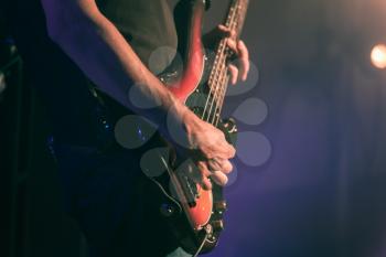 Closeup vintage toned photo of bass guitar player hands, soft selective focus, live music theme, old style effect