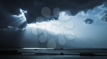 Dark stormy clouds and sunlight, landscape background photo. Cargo ships enter bay of Izmir, Turkey. Blue toned stylized photo