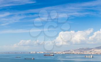 Coastal cityscape with cargo ships under cloudy sky. Izmir city, Turkey