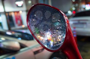 Colorful blurred reflections and raindrops on wet scooter mirror