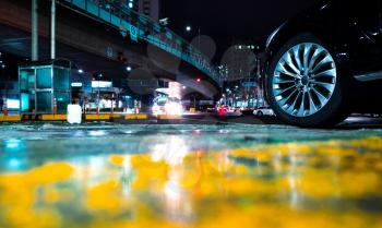 Abstract night street race background with car wheel on wet urban asphalt road with reflections