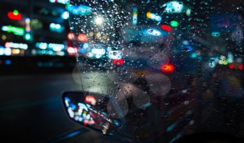 Abstract night city blurred background, colorful reflections and raindrops on wet scooter windscreen
