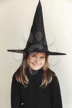 Smiling little blond girl in black witch costume over white wall, close-up studio portrait