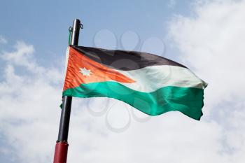 Flag of Jordan waving on wind over cloudy blue sky