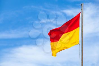 Red and yellow warning flag on a beach over blue sky background